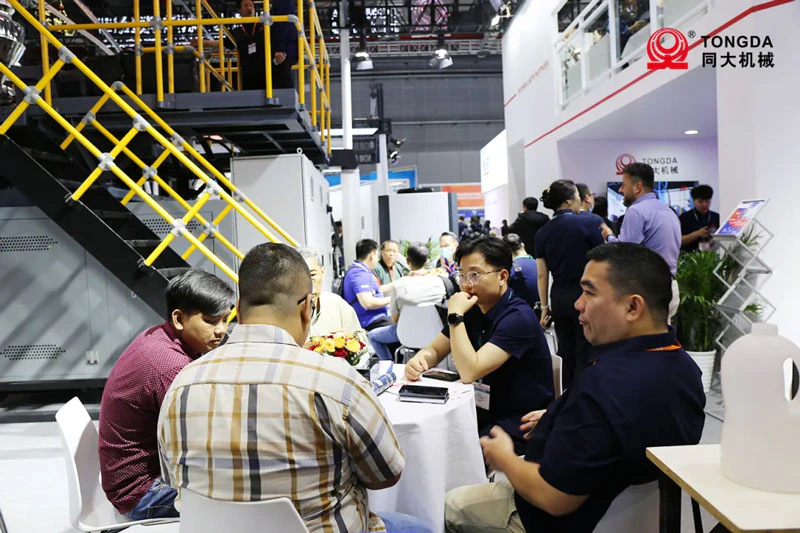 Visitantes con personal de Tongda junto a una sopladora en CHINAPLAS 2024